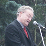 Friedrich Schorlemmer im Anzug mit roter Krawatte am Mikrofon, im Hintergrund Wald